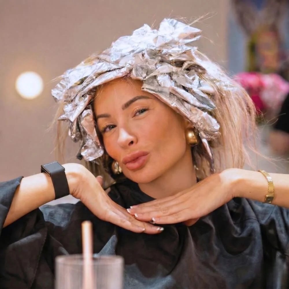 A smiling woman sitting in a hair salon chair with colour foils processing in her hair
